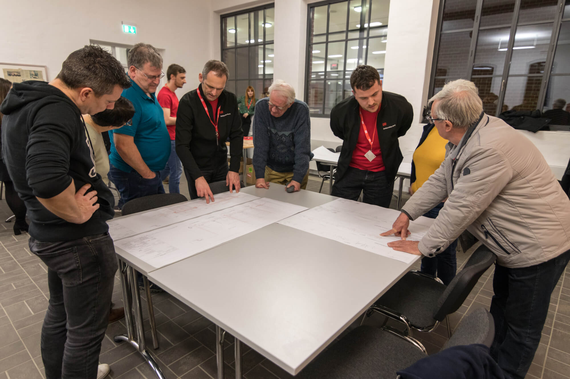2 DB-Mitarbeiter erklären 6 Interessierten Plände die auf einem Tisch liegen