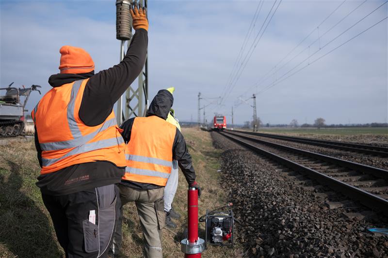 Zwei Bauarbeiter stehen am Gleis und winken der einfahrenden S-Bahn zu.